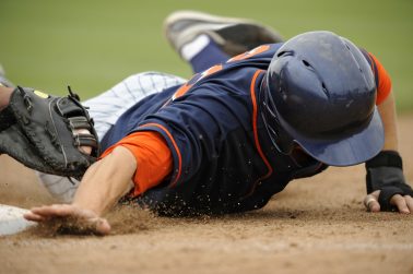 A Baseball player dives back to first base.